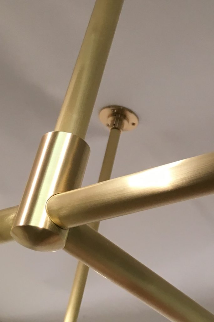 Close-up view of a modern brass ceiling pot racks, attached to a smooth white ceiling. The fixture has a sleek and minimalist style, showcasing a polished metallic finish.