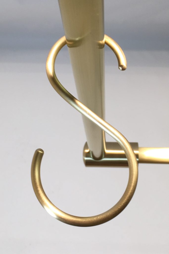 Close-up of a brass metal hook shaped like the letter S on a pot racks rod. The elegant hook is perfect for holding kitchen essentials and stands out beautifully against the plain background.