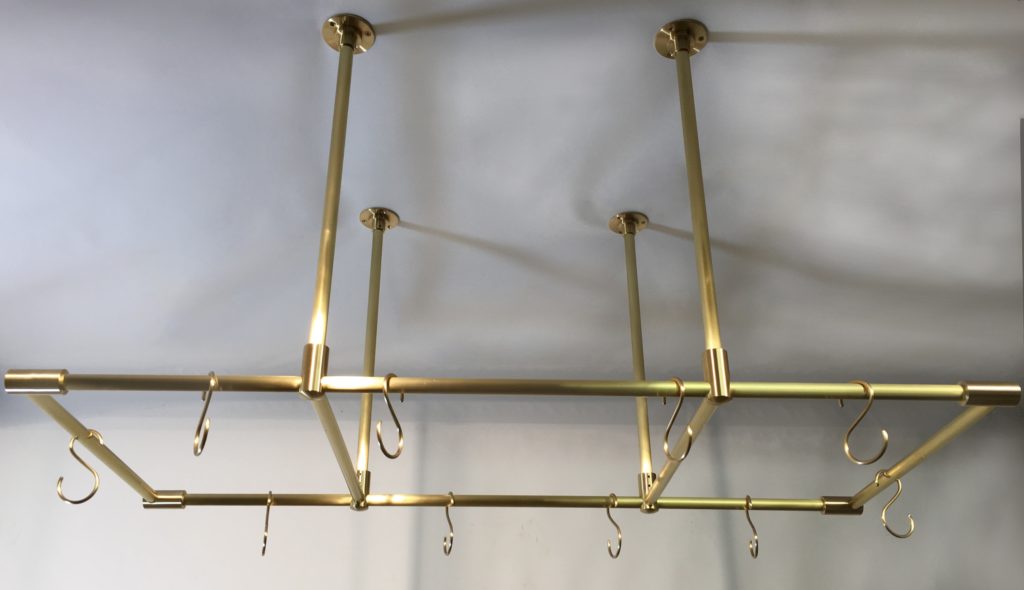 A rectangular brass pot rack mounts seamlessly on the ceiling with multiple hooks. Vertical rods connect a sleek horizontal frame, while its elegant brass finish adds a touch of sophistication against the plain background.