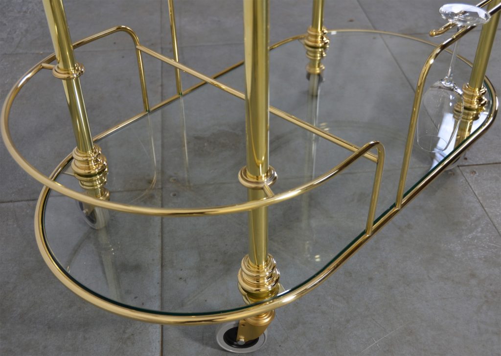 A custom made polished brass champagne trolley with glass shelves.