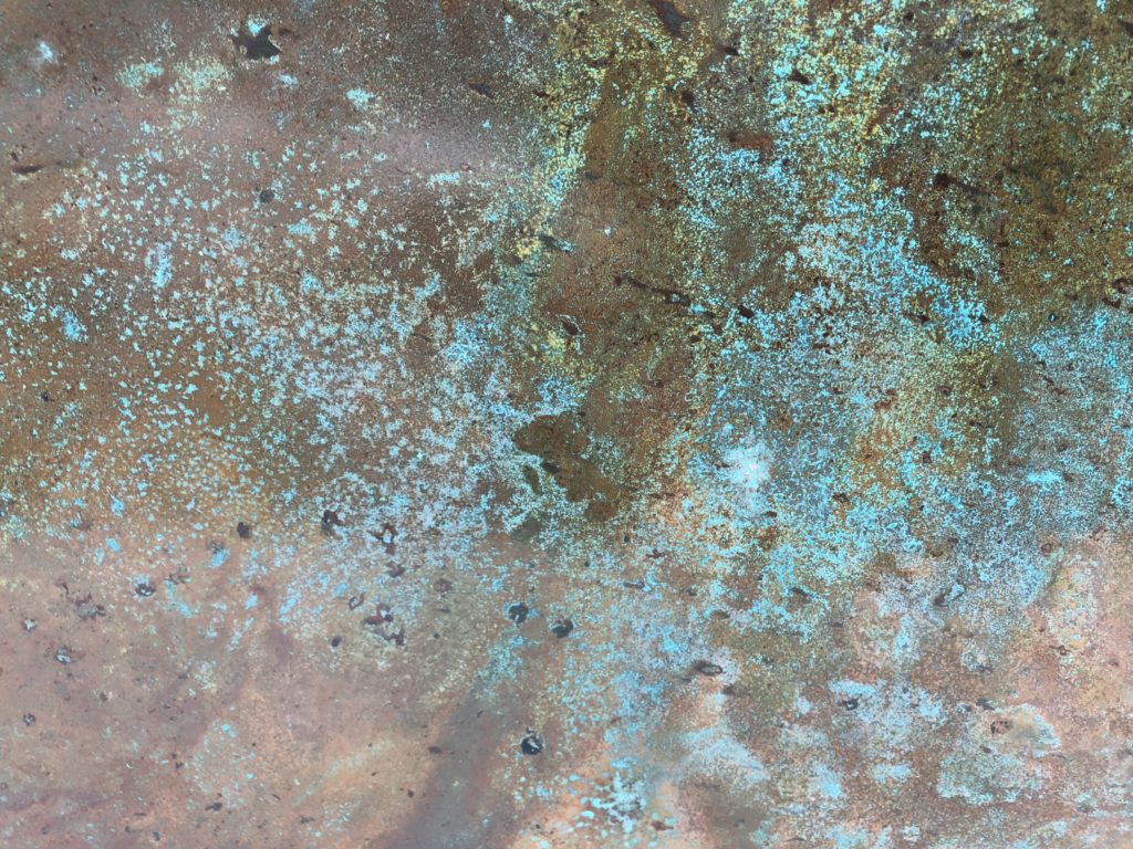 Rustic patinated copper panels with patches of turquoise and brown, resembling. The texture shows oxidization or corrosion, with subtle gradients and speckled areas creating an abstract, weathered appearance.