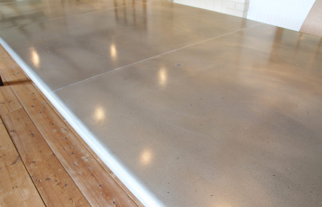 A shiny, polished custom zinc dining table with a smooth finish is placed on a wooden floor.