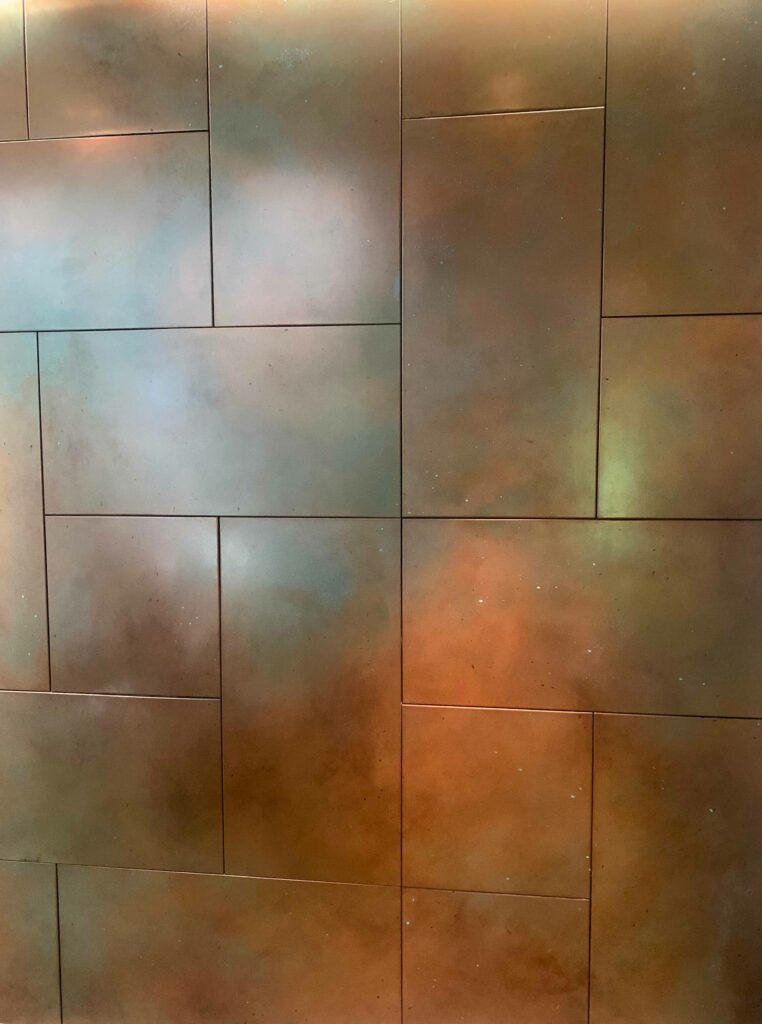 A close-up image showcases copper wall paneling arranged in a grid-like pattern, featuring a patina with gradient shades of brown, green, and blue.