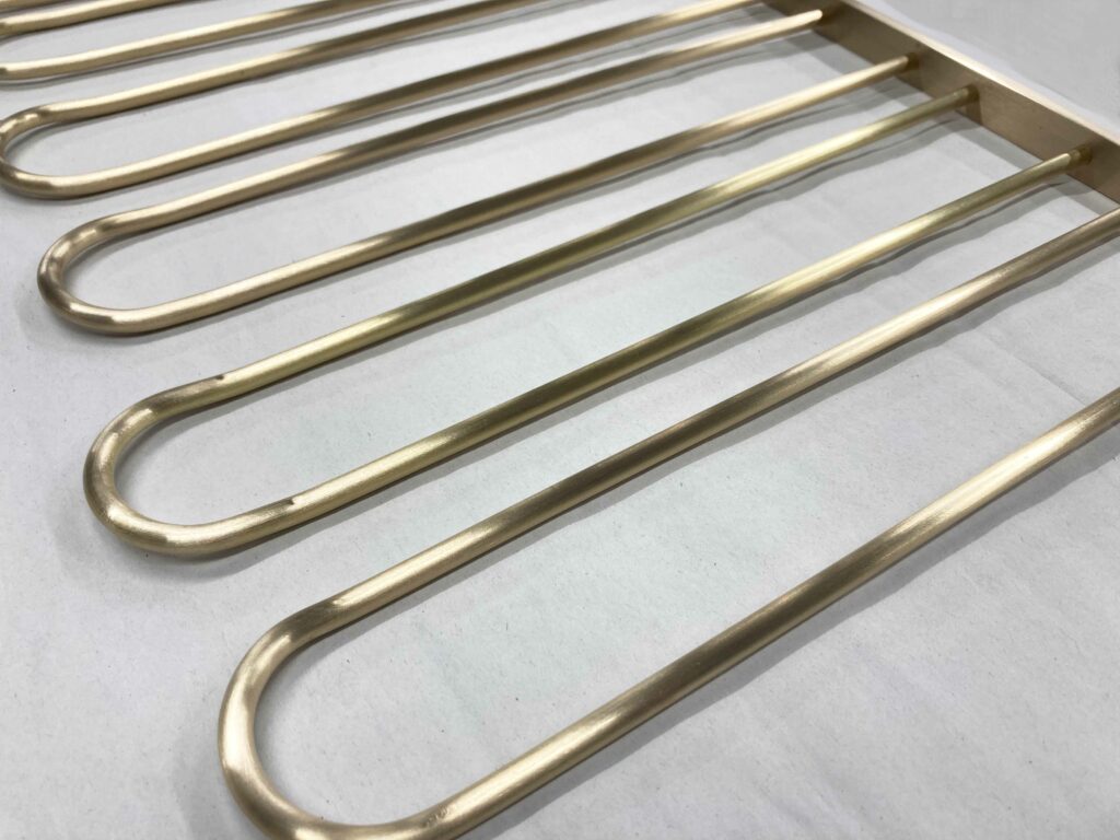 A close-up of a brass stemware holder on a white surface. The rack has multiple evenly spaced parallel bars.