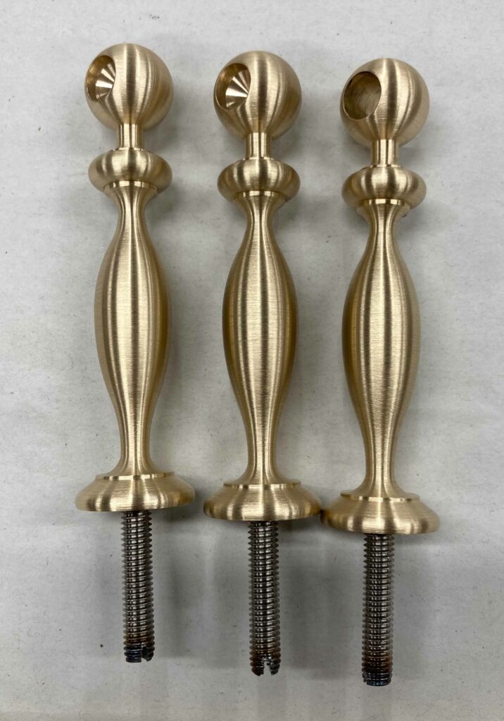 Three metallic bar back shelf components with a brushed finish are arranged vertically against a neutral backdrop. Each finial has a spherical top and a threaded base for attachment.