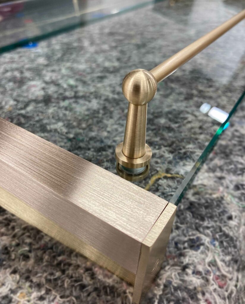 Close-up of a glass shelf with a brass railing and detailed metallic framework, resting on a textured, speckled surface.