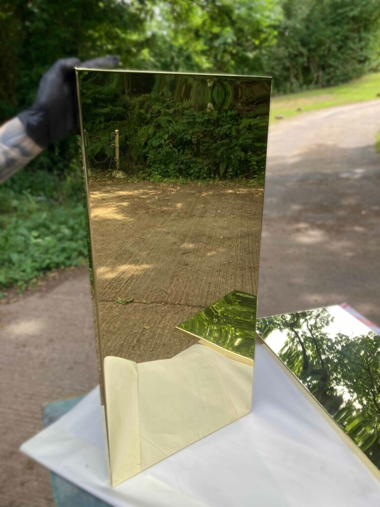 A shiny, reflective polished brass kitchen cupboard doors against greenery and a concrete path.