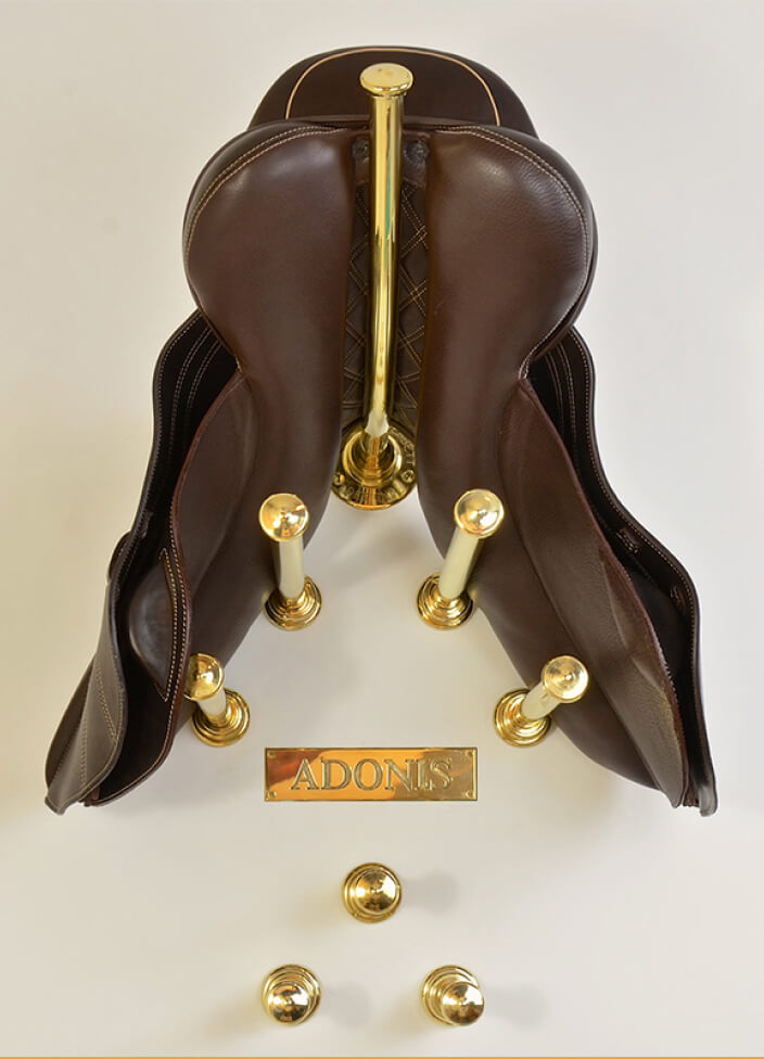 A polished brass saddle rack with a curved, elegant design is mounted on a wall. Its durable construction and sleek finish highlight both functionality and timeless style in an equestrian setting.