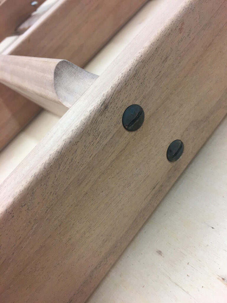 Close-up of a wooden library ladder step with a smooth, light finish. It features two metal screws fastened into one of the wooden panels.