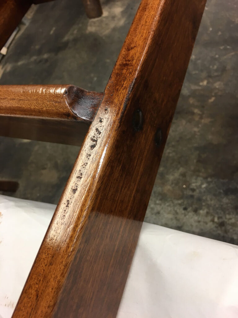 Close-up of a wooden library ladder with a glossy finish. The wood is dark brown with visible grains and a few scuff marks. The background is a blurry gray and white surface.