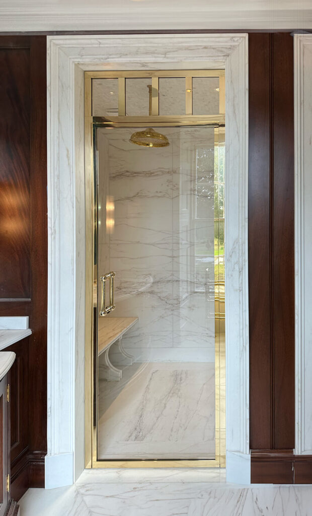 Luxurious bathroom featuring a marble shower with a bespoke brass shower screen. The interior has a built-in bench and a ceiling-mounted showerhead.